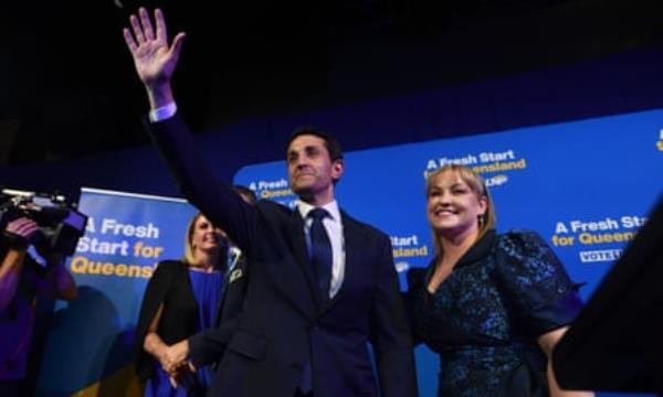 David Crisafulli, in a suit and tie, waves with his wife Tegan wearing a dark blue dress at his victory party in Brisbane