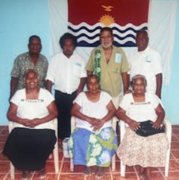 Seven members of the Kiritimati Association of Atomic Cancer Patients in front of the island's flag.